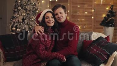 <strong>一家人</strong>坐在家中圣诞树附近的沙发上的年轻幸福。 庆祝<strong>新年</strong>的情侣